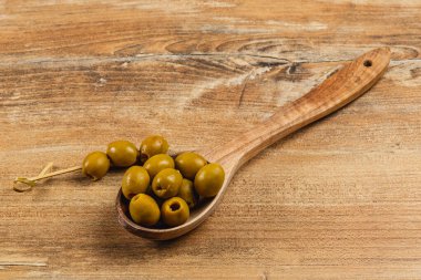 Ahşap bir kaşık, zengin renklerini ve dokusunu kırsal bir ahşap arka planda sergileyen birkaç yeşil zeytin barındırır. Yemek sunumlarını ve yemekleri geliştirmek için mükemmel..