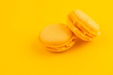 Mükemmel işlenmiş iki sarı badem kurabiyesi canlı sarı bir arka fona karşı yan yana oturur, pürüzsüz dokularını ve hoş dolgularını sergilerler, her tatlı aşığı için mükemmeldir..