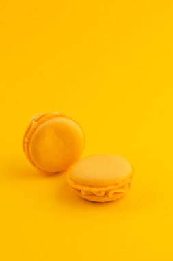 İki sarı badem kurabiyesi canlı sarı bir arkaplanda dinleniyor. Narin dokularını ve pürüzsüz dolgularını sergiliyorlar. Zarif bir tatlı sunumu için mükemmel..