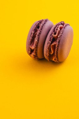 İki zengin çikolatalı makarna yan yana oturur. Narin dokularını ve kremsi dolgularını parlak sarı bir zemin üzerinde sergilerler. Görsel cazibelerini arttırırlar..