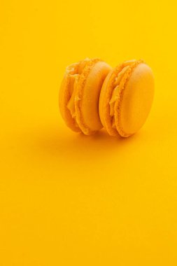İki sarı badem kurabiyesi, parlak sarı bir arka planda yan yana oturur, pürüzsüz dokularını ve kremsi dokularını sergilerler, tatlı bir tat deneyimini davet ederler..