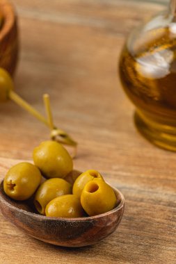 Taze yeşil zeytinler, ahşap bir kasede, bir şişe zeytinyağı eşliğinde, ahşap bir masa üzerinde davetkar ve basit bir mutfak vitrini oluşturur..