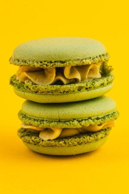 Kremalı iki desenli yeşil badem kurabiyesi parlak sarı bir arkaplanda oturup pürüzsüz dokularını ve davetkar renklerini sergiliyorlar. Tatlı severler için ideal..