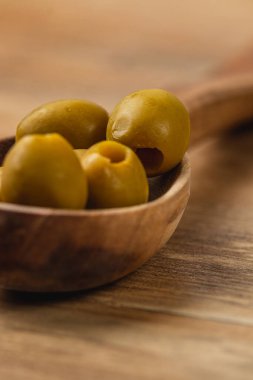 Taze yeşil zeytinler el yapımı ahşap bir kaşıkta dinleniyor, yumuşak ve sıcak bir zemin üzerine doğal renklerini ve dokularını vurguluyorlar. Bu ayar kırsal bir basitlik hissi uyandırıyor..