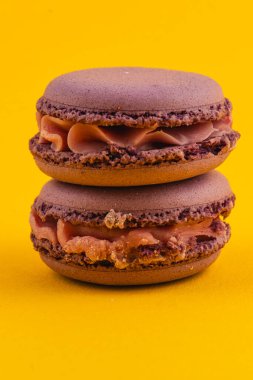 Kremalı karamelli iki lezzetli çikolatalı makarna, zengin dokularını ve renklerini sergileyerek, koyu sarı bir zemin üzerinde yan yana otururlar..