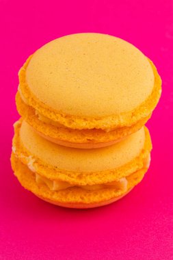 İki altın sarısı badem kurabiyesi düzgün bir şekilde üst üste istiflenerek zarif dokularını parlak pembe bir zemin üzerinde sergiliyorlar ve çarpıcı bir görsel karşıtlık yaratıyorlar..