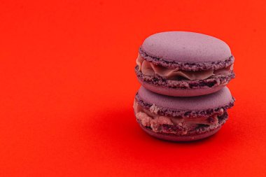 İki yumuşak mor badem kurabiyesi yan yana oturur ve parlak kabuklarını ve kremsi dolgularını sergilerler. Canlı turuncu arka plan cazibelerini arttırıyor..