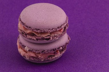 İki mor badem kurabiyesi, parlak mor bir arka plana karşı güzelce istiflenir. Narin kurabiyeler kremalı, gösterişli enfes bir dokuya ve renge sahiptir..