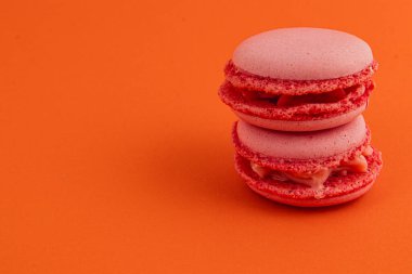 Kremalı iki pembe badem kurabiyesi parlak turuncu bir zemine karşı güzelce istiflenmiş, desenli kabuklarını ve davetkar renklerini sergiliyorlar..