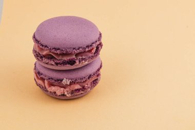 Çikolata ganache ile dolu iki mor badem kurabiyesi pürüzsüz sarı bir zemin üzerinde zarif bir şekilde istiflenir ve görsel olarak çekici ve minimalist bir görüntü oluşturur..