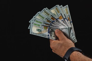 A hand is confidently displaying a fan of hundred dollar bills against a stark black background, emphasizing the value of cash and financial wealth.