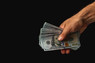 A hand displays multiple stacks of hundred dollar bills on a dark background, highlighting the details of the currency and the act of holding money.