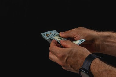 Hands hold and count paper currency in low light, creating a dramatic contrast. The focus on the cash suggests a moment of transaction or contemplation.