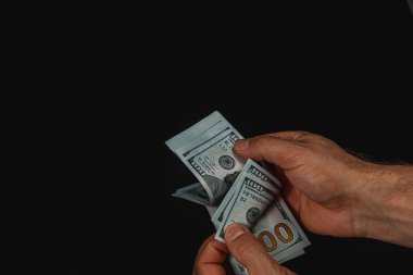 Two hands are seen counting several hundred dollar bills in a dimly lit environment, suggesting a financial transaction may be taking place.