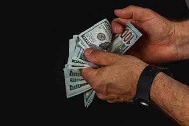 Hands skillfully gather and count several hundred dollar bills against a dark backdrop. The money appears crisp and well-organized, showcasing the denominations clearly.