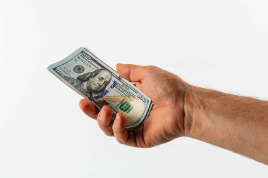 A hand extends forward, firmly grasping a one hundred dollar bill. The bill is clearly visible against a neutral backdrop, emphasizing its details and texture.