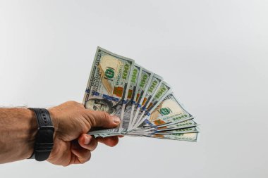 A hand prominently displays several one hundred dollar bills against a plain background. The money appears crisp and well-organized, showcasing its value.