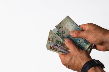 Hands hold a mix of banknotes from different denominations against a neutral background, showcasing the texture and design of the currency being counted.
