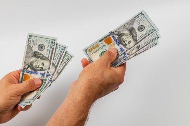Hands holding multiple banknotes of different denominations, carefully counting and transferring currency in a neutral indoor setting with plain background.
