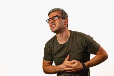 A man is experiencing discomfort while standing against a light background. He holds his chest with one hand, showing a pained expression.