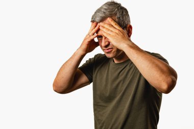 A middle-aged man stands against a neutral background, visibly stressed and holding his head in frustration, conveying a sense of emotional struggle.