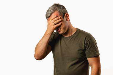 A man stands in a relaxed posture, covering his face with one hand, conveying a sense of frustration. He appears deep in thought in a minimal setting.