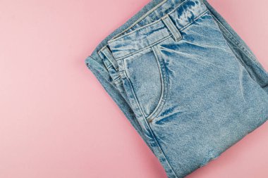 Denim kotları düzgünce katlanır ve yumuşak pembe bir yüzeye yerleştirilir, açık mavi renkleri ve günlük tarzları sergilenir. Moda tutkunları için ideal.