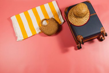 İçinde bir valiz, bir dokuma çantası ve pembe bir yüzeye yerleştirilmiş çizgili bir plaj havlusu olan canlı bir kurgu. Yaz yolculuğu ve plaj günleri için mükemmel..