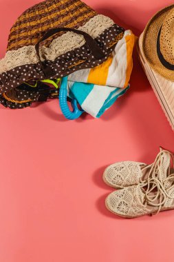 Renkli bir plaj çantası havlu ve aksesuarlarla doludur. Pembe bir yüzeye yerleştirilir. Güneş altında eğlenceli bir güne hazır el yapımı sandaletlerle..