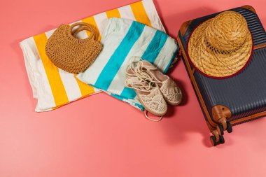 Plaja hazır bir kurulumda bir bavul, dokuma çantası, sandaletler, havlular ve parlak pembe arka planda bir hasır şapka, güneşli bir kaçış için mükemmel..