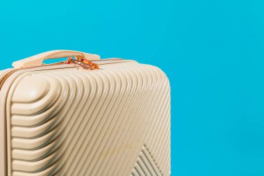Açık krem renginde modern, desenli bir bavul canlı bir mavi arkaplanda duruyor, parlak tasarımı ve seyahate hazır görüntüsüyle..