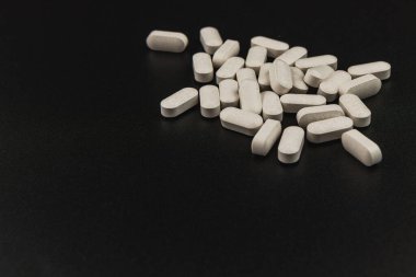 Beyaz tabletler siyah bir yüzeye rastgele dağılmış. İlaç formlarını vurguluyorlar. Düzenleme sağlık ve sağlığın önemini vurguluyor.