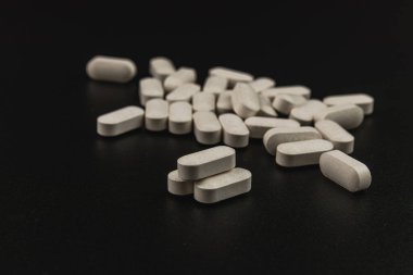 Multiple white tablets are scattered across a black surface, showcasing their oval shape and texture in a dramatic contrast against the dark background.