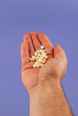 A hand with an open palm holds a collection of small white pills, contrasting vividly with a flat blue background. The setting highlights the texture and details of the pills.