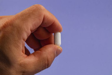 A hand is holding a white pill, positioned against a soft purple background, illustrating a focus on healthcare and medication practices.