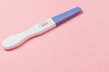 A pregnancy test displays two lines, indicating a positive result. The test is placed on a soft pink background, highlighting its features.
