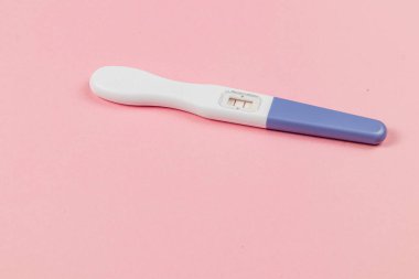 A pregnancy test lies on a soft pink surface, clearly indicating positive results. The setting reflects a moment of anticipation and joyful expectation.