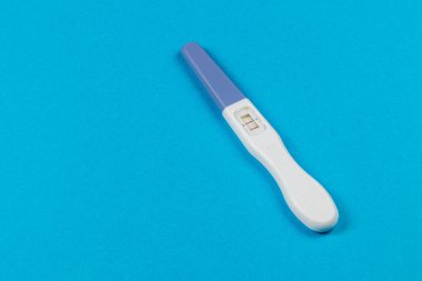 Bir hamilelik testi parlak mavi bir arka planda durur ve sonuçları gösterir. Bu basit ama önemli şey, pek çok ebeveyn için umut ve beklentiyi temsil ediyor..