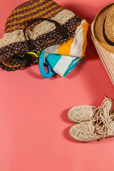 Renkli bir plaj çantası havlu ve aksesuarlarla doludur. Pembe bir yüzeye yerleştirilir. Güneş altında eğlenceli bir güne hazır el yapımı sandaletlerle..