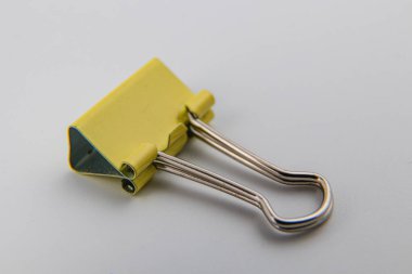 Pürüzsüz beyaz bir yüzeye yerleştirilmiş sarı bir ataç çoklu kağıt tabakalarını güvenli bir şekilde bir arada tutmak için pratik tasarımını gösteriyor..