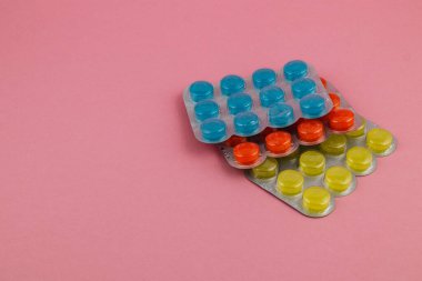 Canlı renkli tabletler içeren çeşitli kabarcık paketleri yumuşak pembe bir arkaplana karşı düzenli olarak düzenlenir, eşsiz şekilleri ve renkleri sergilenir.