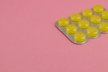 Yakın planda sarı jelatin kapsüller yumuşak pembe arkaplana karşı gümüş bir su toplayıcı pakete yerleştirilerek canlı ve göz alıcı bir kompozisyon oluşturulur..