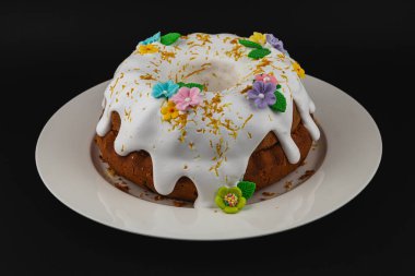 Beyaz kremalı, renkli çiçek süslemeleriyle süslenmiş, yuvarlak bir tabakta, siyah bir arka planda duran güzel bir demet pasta..