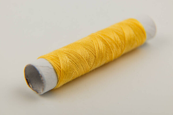 A vibrant yellow spool of sewing thread sits on a clean white surface, showcasing its texture and color, perfect for a variety of crafting and sewing projects.