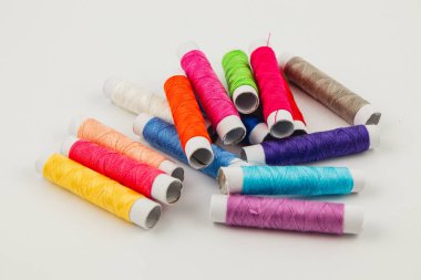 Çeşitli renklerde canlı dikiş iplikleri beyaz bir yüzeye dağılmış, el yapımı, yorgan dikme ve dikiş faaliyetleri için idealdir.