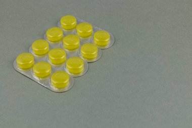 Bright yellow tablets neatly aligned in a plastic blister pack resting on a gray surface, showcasing a clean and organized layout that emphasizes the medication.