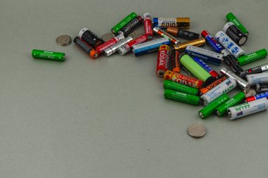 Çeşitli bataryalardan oluşan bir koleksiyon açık gri bir yüzeye yayılır, birkaç madeni paranın yanında. Düzenleme farklı marka ve boyutlarda, renklerini gösteriyor..