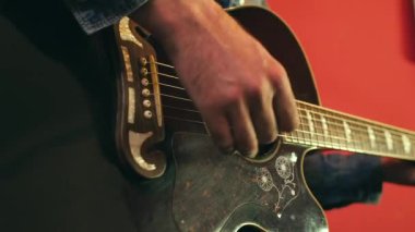 Kırmızı arkaplana karşı akustik gitar çalan bir adamın eli. 