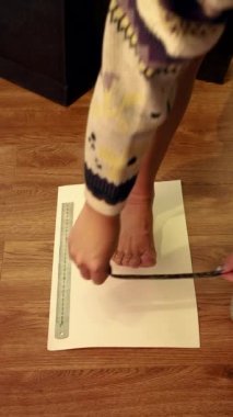 Evde kendi ayağını kalem ve çarşafla ölçmenin doğru yolunu gösteren bir kız.