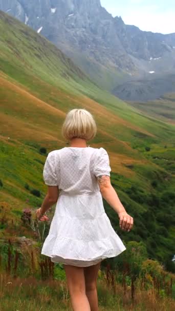 白いドレスのブロンドは山脈のパノラマの中で山を降りる — ストック動画
